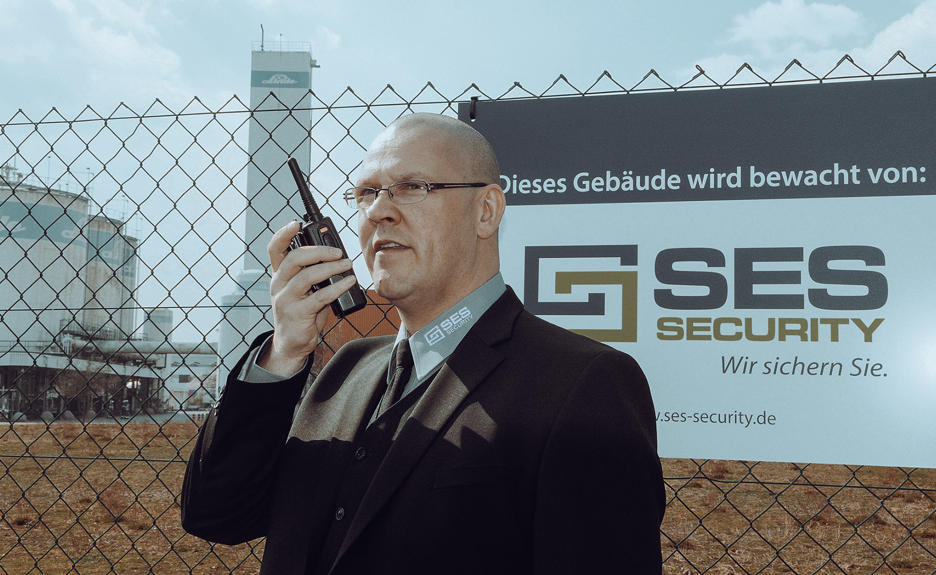 SES Security Mitarbeiter kommuniziert über Funkgerät vor einem Werkschutz-Schild