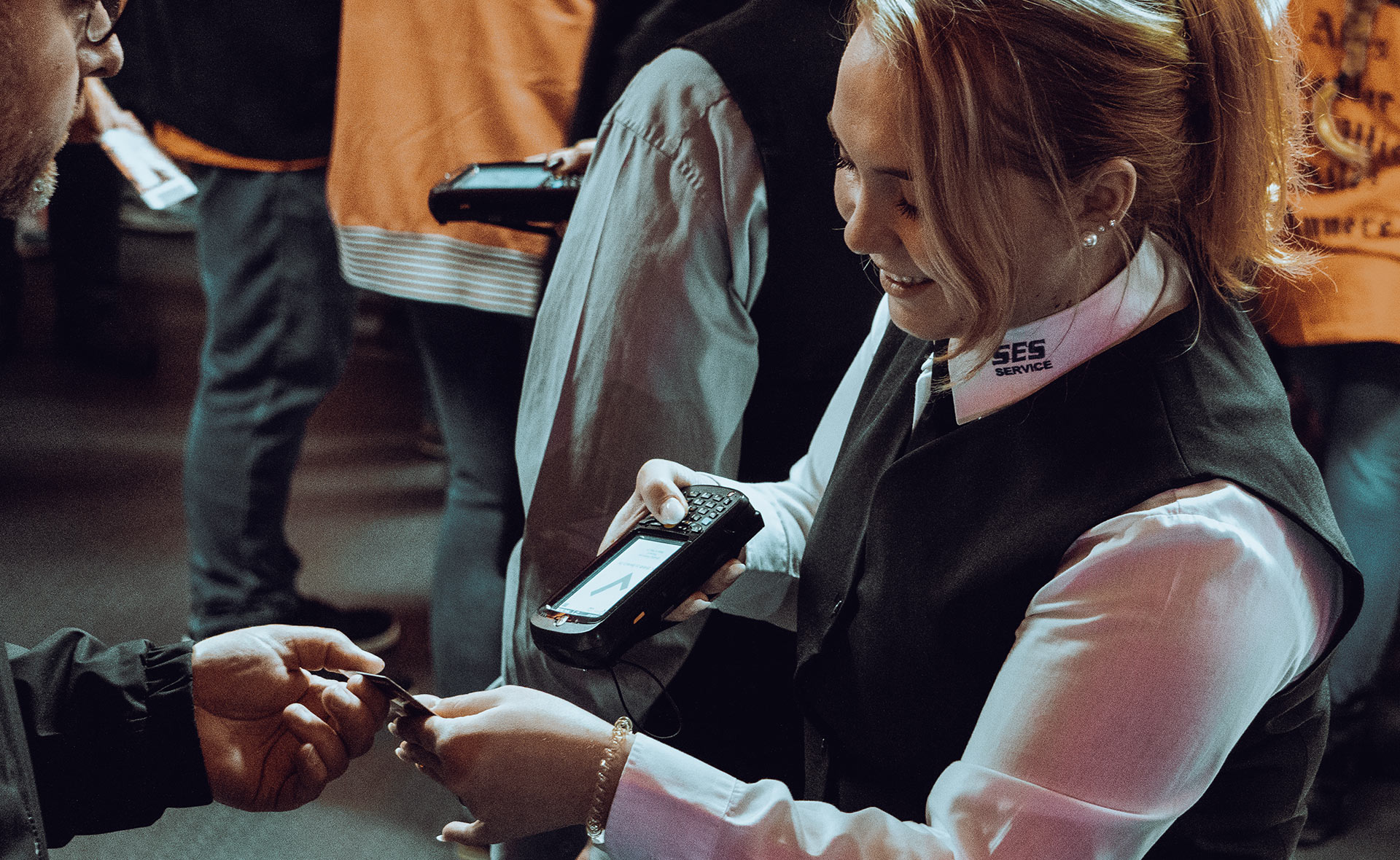 Lächelnde SES Service Mitarbeiterin bedient ein tragbares Zahlungsgerät bei einer Veranstaltung