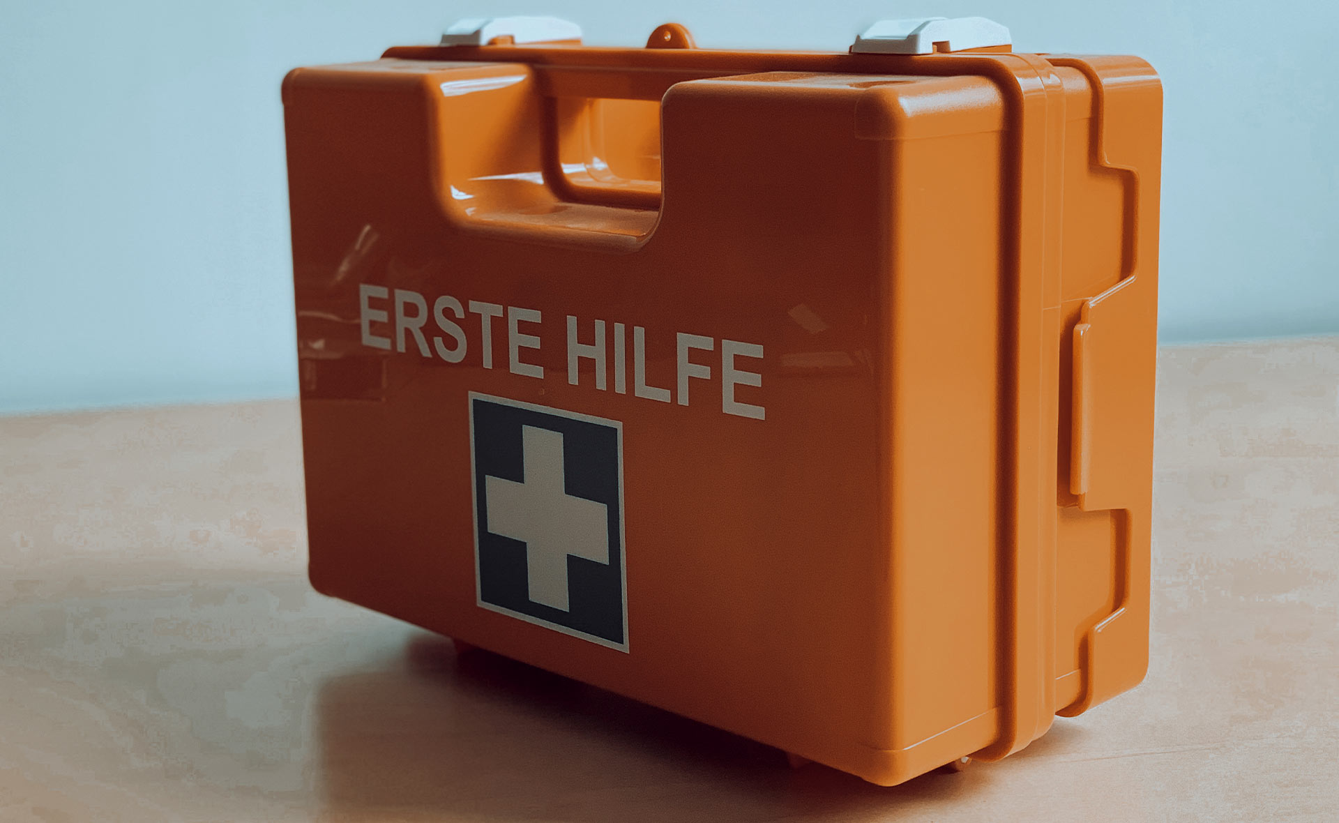 Orangefarbener Erste-Hilfe-Koffer mit dem Schriftzug 'ERSTE HILFE' und einem weißen Kreuz